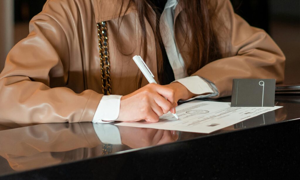 Registration Close-up of a woman signing a document at a sleek reception counter, indoor setting.